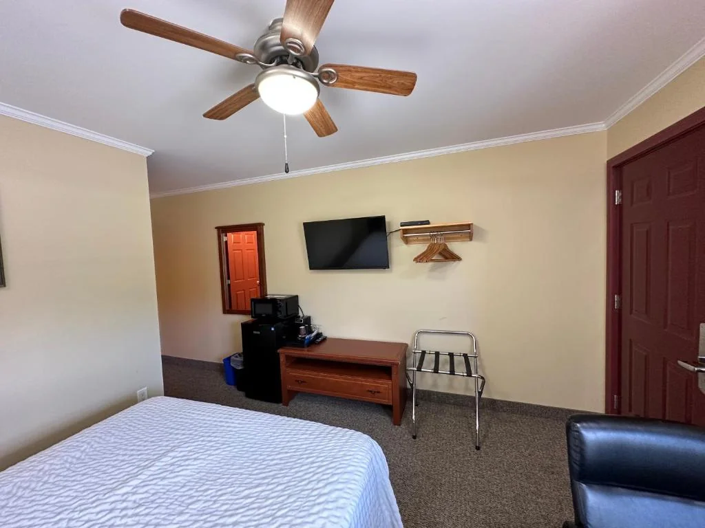 Guest room with a queen bed, wall-mounted TV and ceiling fan